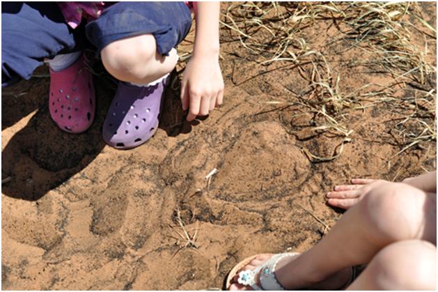 feet of two little girls next to shape of heart drawn in the soil