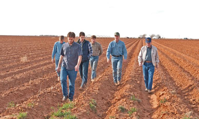 Eddie Bingham and son, Cliff Bingham, walking in their farm field with grandsons, Clint, Kyle, Blake, and Nathan.